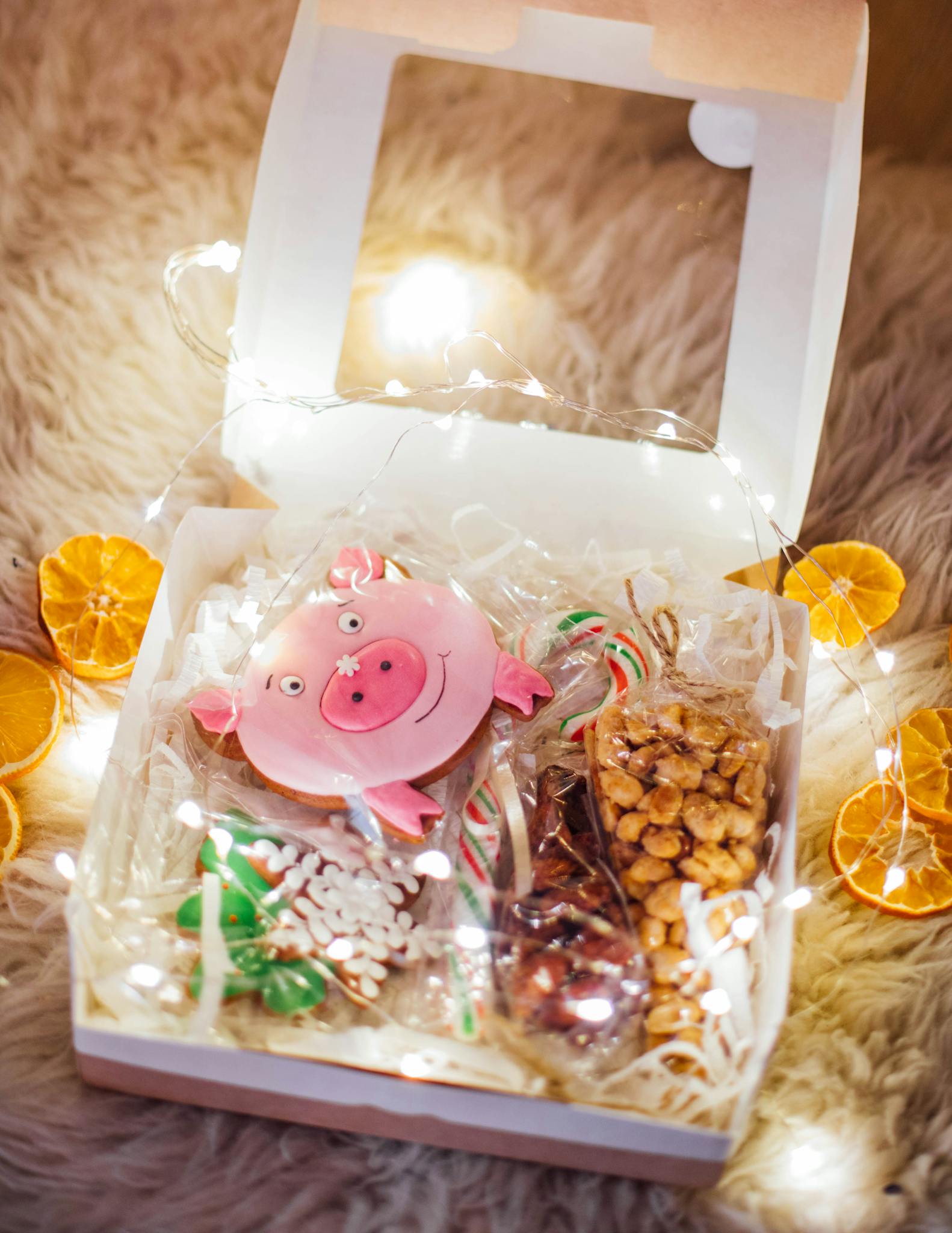 A cozy box of assorted holiday treats adorned with festive string lights and dried oranges.