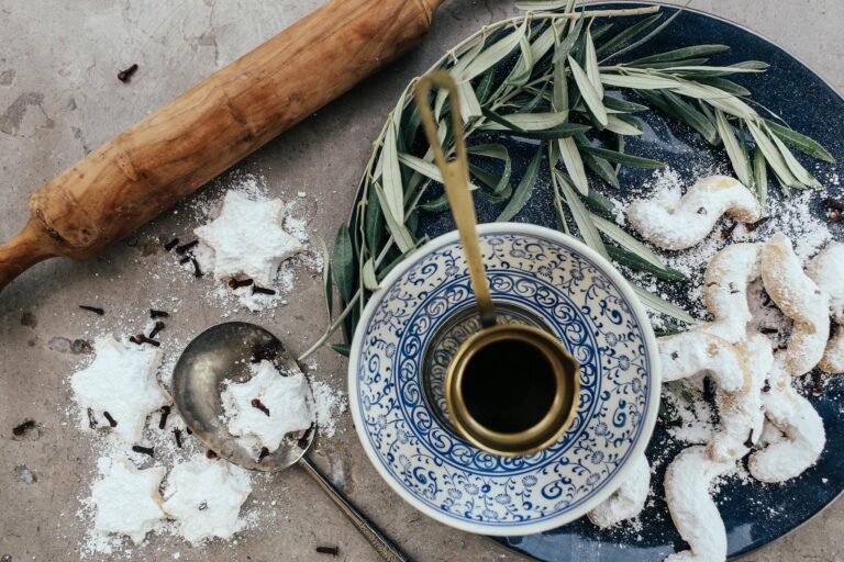 A rustic baking setup with powdered sugar biscuits and a brass cup on a blue plate.