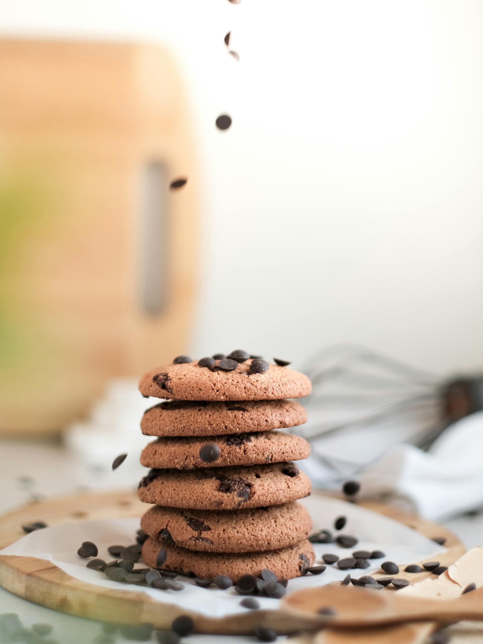 A vertical shot of a stack of chocolate chip cookies with chips falling around them.