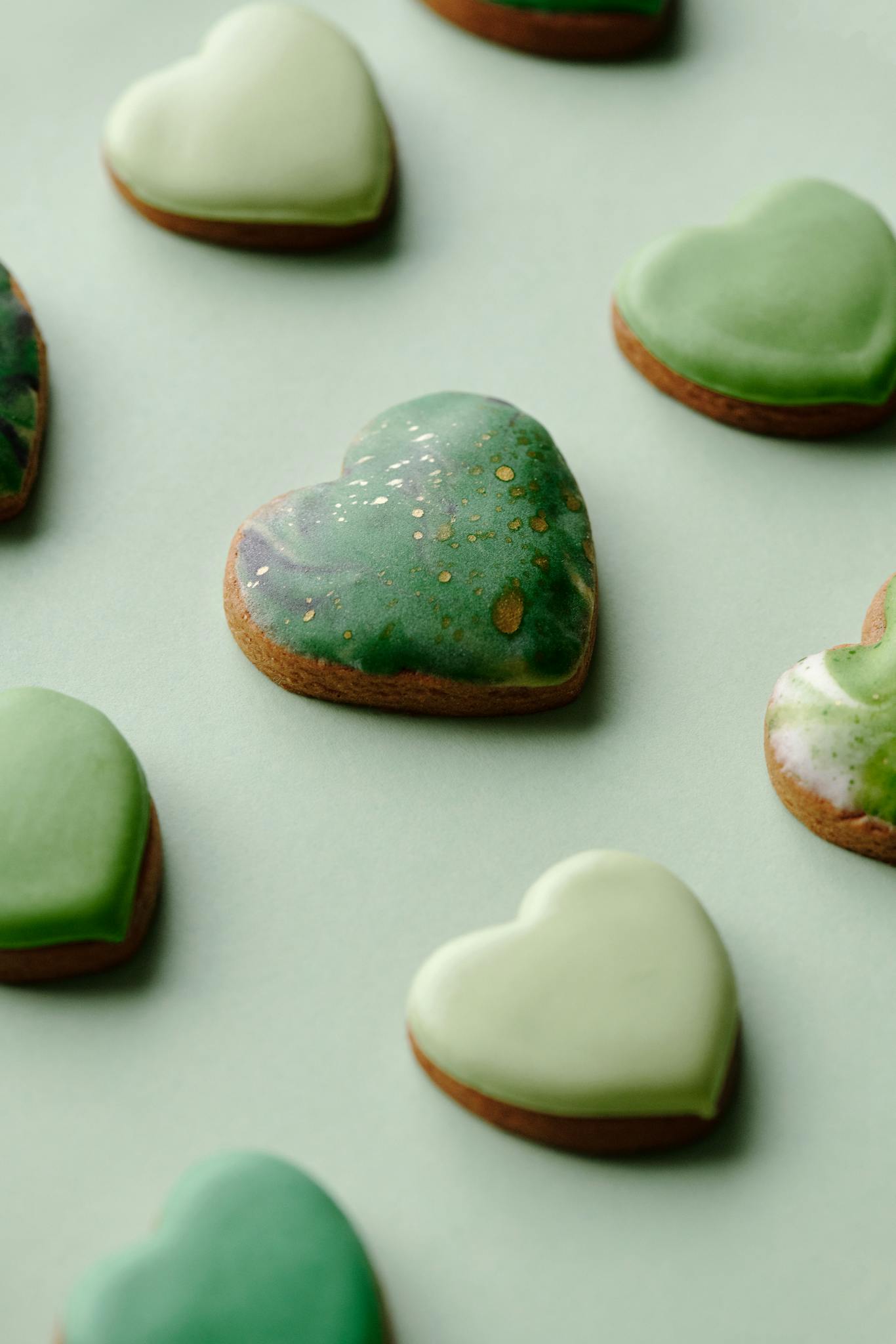 Assorted heart-shaped cookies with green icing on a pastel background, perfect for a sweet treat.
