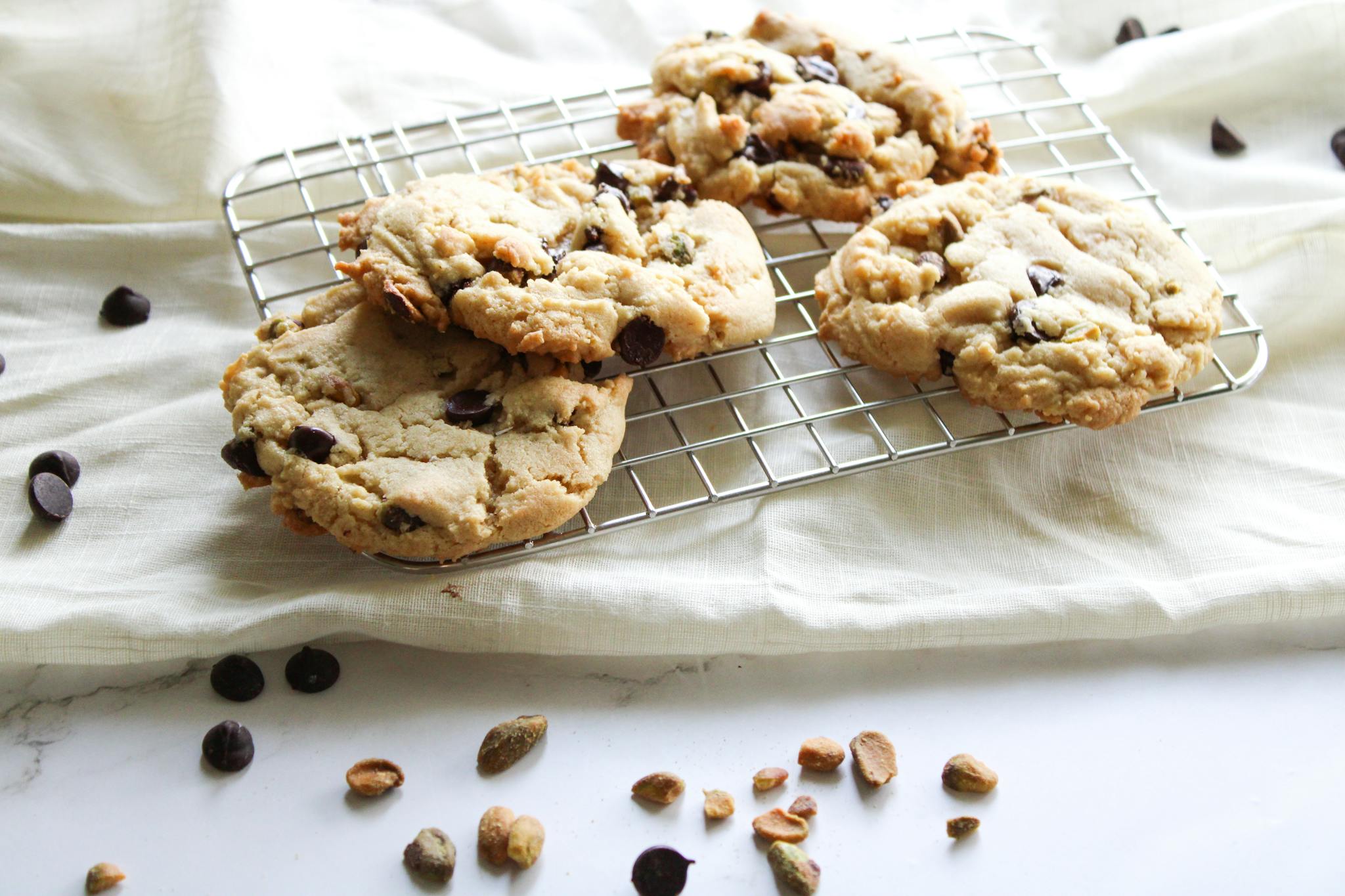 Close-up of freshly baked chocolate chip cookies on a cooling rack with scattered nuts.