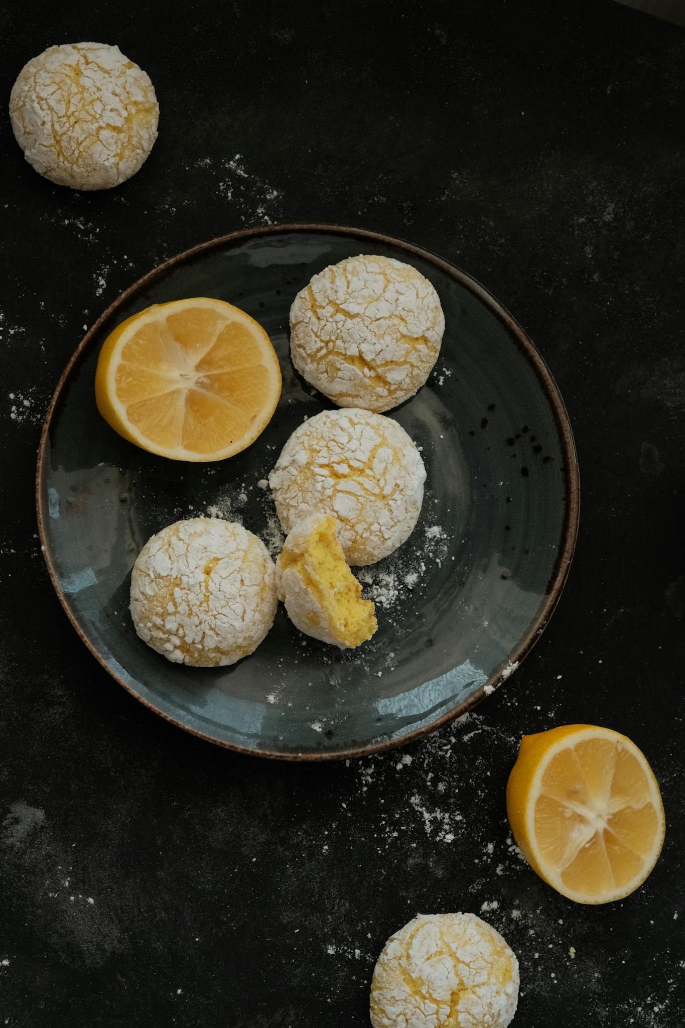 Crinkly lemon cookies on a dark plate with sliced lemons, food photography.