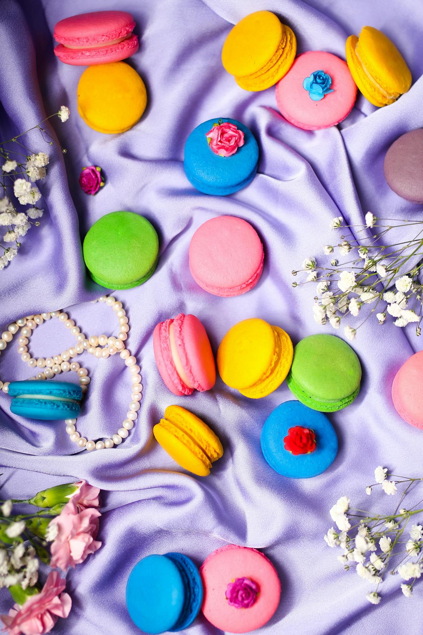 Vibrant macarons arranged on lavender fabric with delicate flowers and pearls.